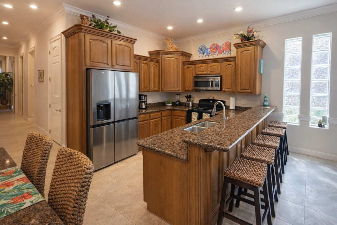 Modern kitchen with granite counters, stainless steel appliances, woven barstools, and vibrant decor. Bright, spacious layout ideal for cooking, entertaining, and relaxing. Natural light and stylish touches throughout.