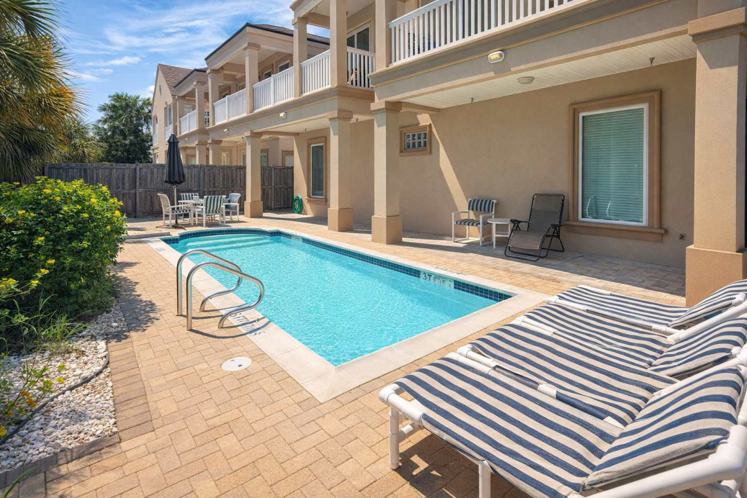 Relax in your dashing courtyard oasis featuring a sparkling pool, striped loungers, shaded dining, and beach-style balconies—perfect for sun-soaked getaways and family-friendly stays near the coast.