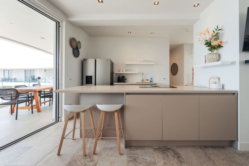 This sleek, modern kitchen features a minimalist design with a large island, stainless steel appliances, and stylish bar stools. Enjoy seamless indoor-outdoor living with access to a spacious balcony.